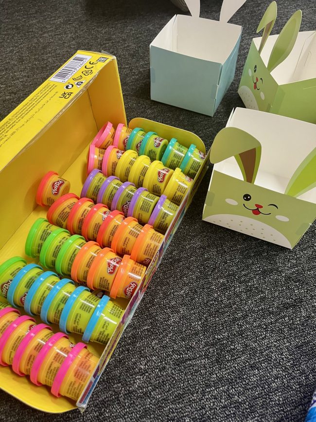 A large pack of Play-Doh cans next to empty bunny cardboard Easter Baskets.