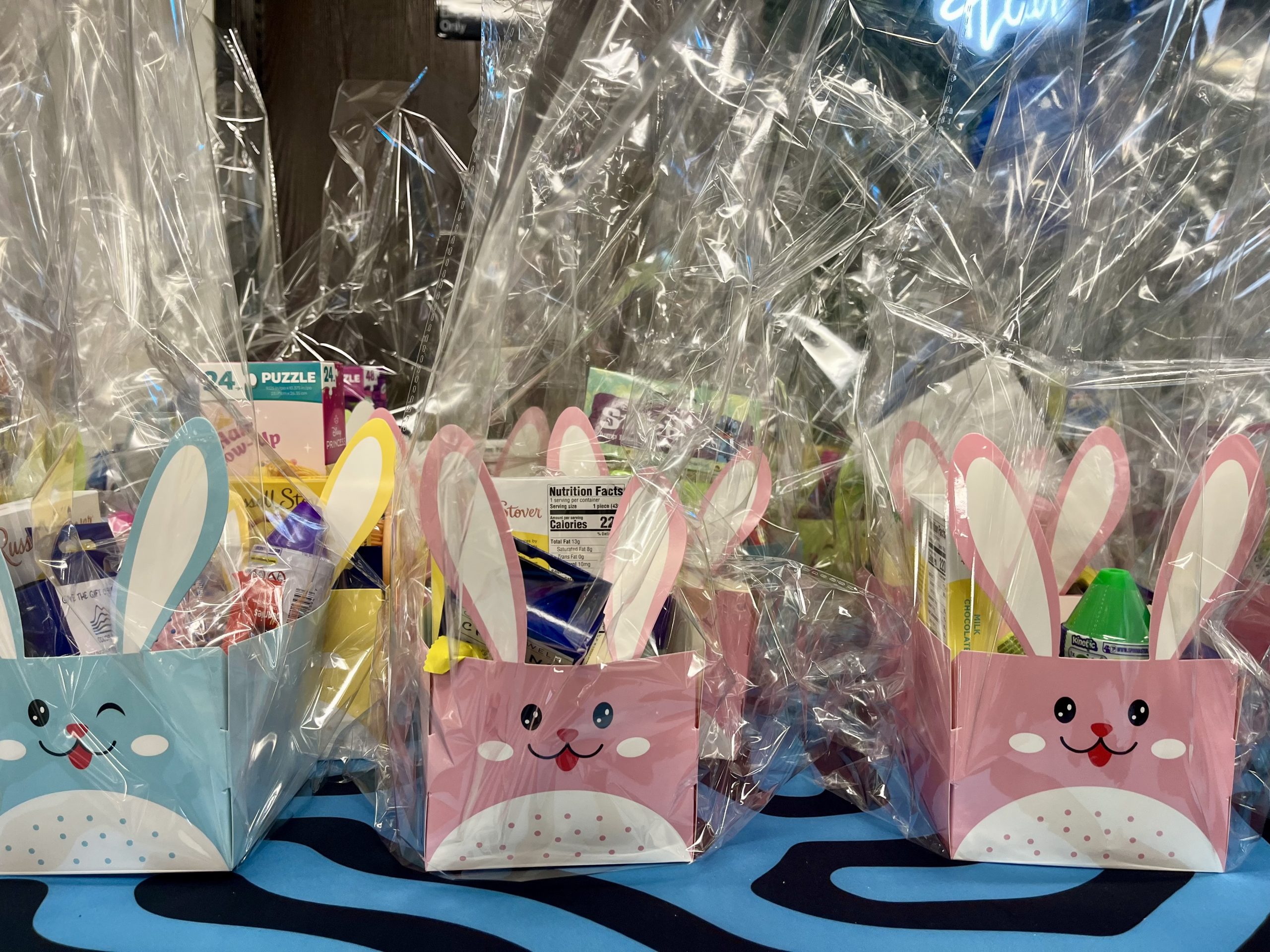 Pink and blue bunny cardboard Easter baskets. The baskets are full of gifts and are wrapped in plastic.